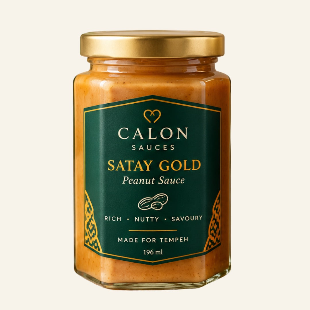 A glass jar of Calon Tempeh Sauces Satay Gold Peanut Sauce with a gold lid and a dark green label, set against a solid off-white background. Perfect for cooking with fresh tempeh.