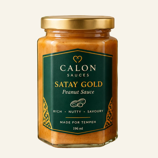 A glass jar of Calon Tempeh Sauces Satay Gold Peanut Sauce with a gold lid and a dark green label, set against a solid off-white background. Perfect for cooking with fresh tempeh.