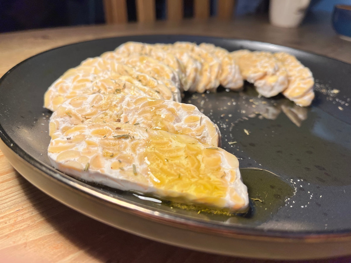 Fresh tempeh, sliced and seasoned. Tastes mild, nutty, slightly earthy, and savoury with umami notes