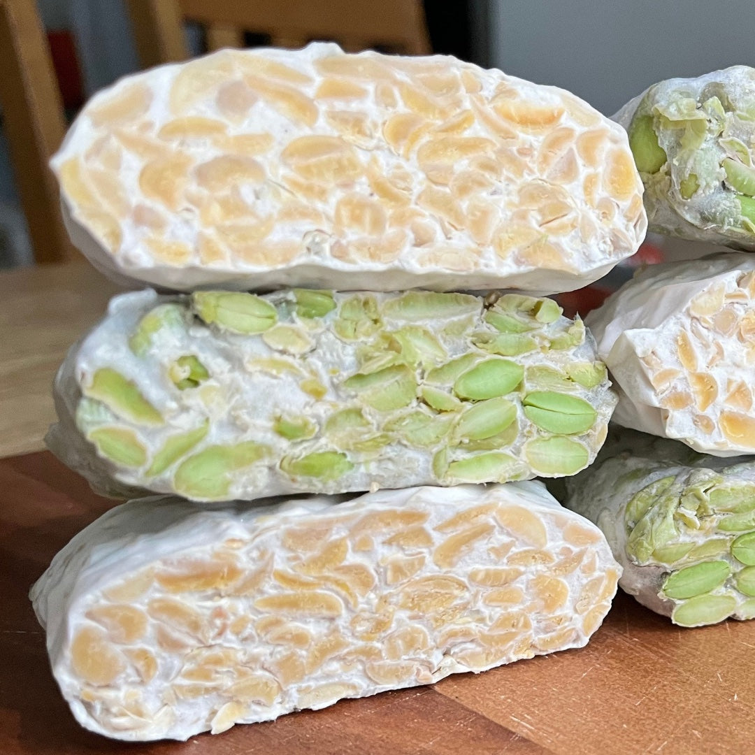 Three stacked slices of sliced tempeh. tempeh made from soybeans and edamame beans. A picture showing the fresh tempeh cuts. You can a fine white network of mycelium grows through the beans and binds them together.